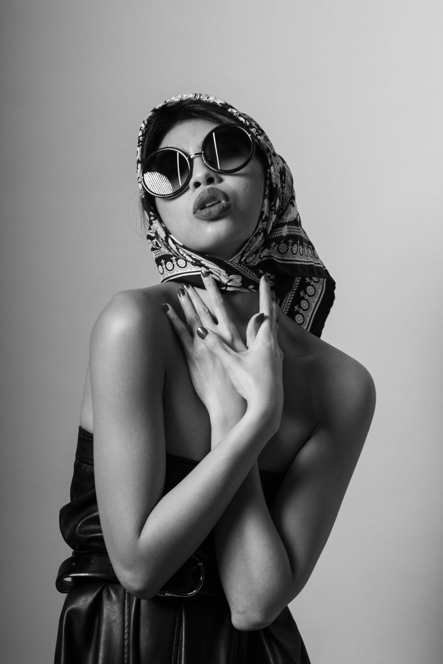 Black and white portrait of a stylish woman in sunglasses and scarf, exuding elegance.
